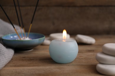 Photo of Burning candle, spa stones and incense sticks on wooden table, closeup