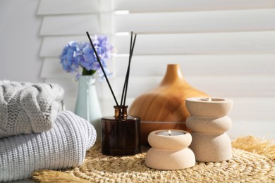Photo of Spa composition with burning candles, aroma oil diffuser and reed air freshener on wicker mat indoors, closeup