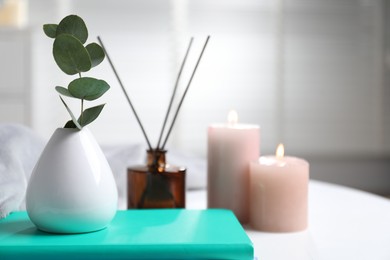 Photo of Spa composition with eucalyptus branch in vase and book on white table indoors, closeup