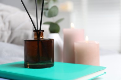 Photo of Spa composition with reed air freshener and book indoors, closeup