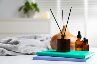 Photo of Spa composition with reed air freshener, cosmetic products and books on white table indoors, closeup