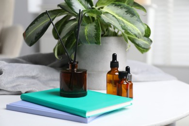 Photo of Spa composition with reed air freshener, cosmetic products and books on white table indoors, closeup