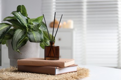 Photo of Spa composition with reed air freshener, books and houseplant on white table indoors, closeup. Space for text