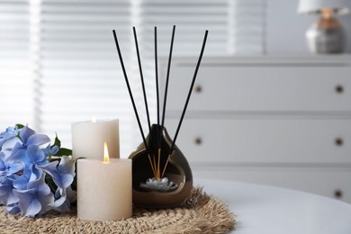 Photo of Spa composition of holder with incense sticks, burning candles and flowers on white table indoors, closeup