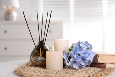 Photo of Spa composition of holder with incense sticks, burning candles and flowers on white table indoors, closeup