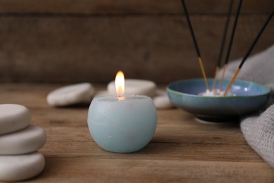 Photo of Burning candle, spa stones and incense sticks on wooden table, closeup