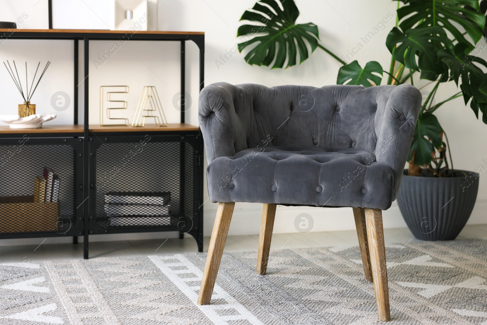 Photo of Stylish grey armchair, shelving unit and houseplant indoors. Interior design