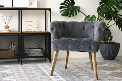 Photo of Stylish grey armchair, shelving unit and houseplant indoors. Interior design