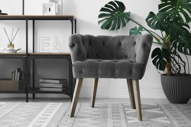 Photo of Stylish grey armchair, shelving unit and houseplant indoors. Interior design