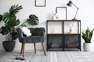 Photo of Stylish grey armchair, shelving unit and houseplants indoors. Interior design