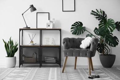 Photo of Stylish grey armchair, shelving unit and houseplants indoors. Interior design