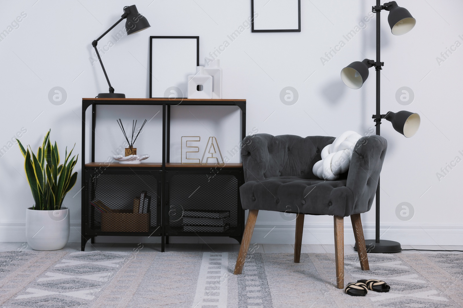 Stylish grey armchair, shelving unit and houseplants indoors. Interior design Photo of Stylish grey armchair, shelving unit and houseplants indoors. Interior design