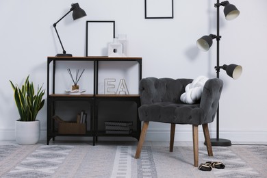 Photo of Stylish grey armchair, shelving unit and houseplants indoors. Interior design