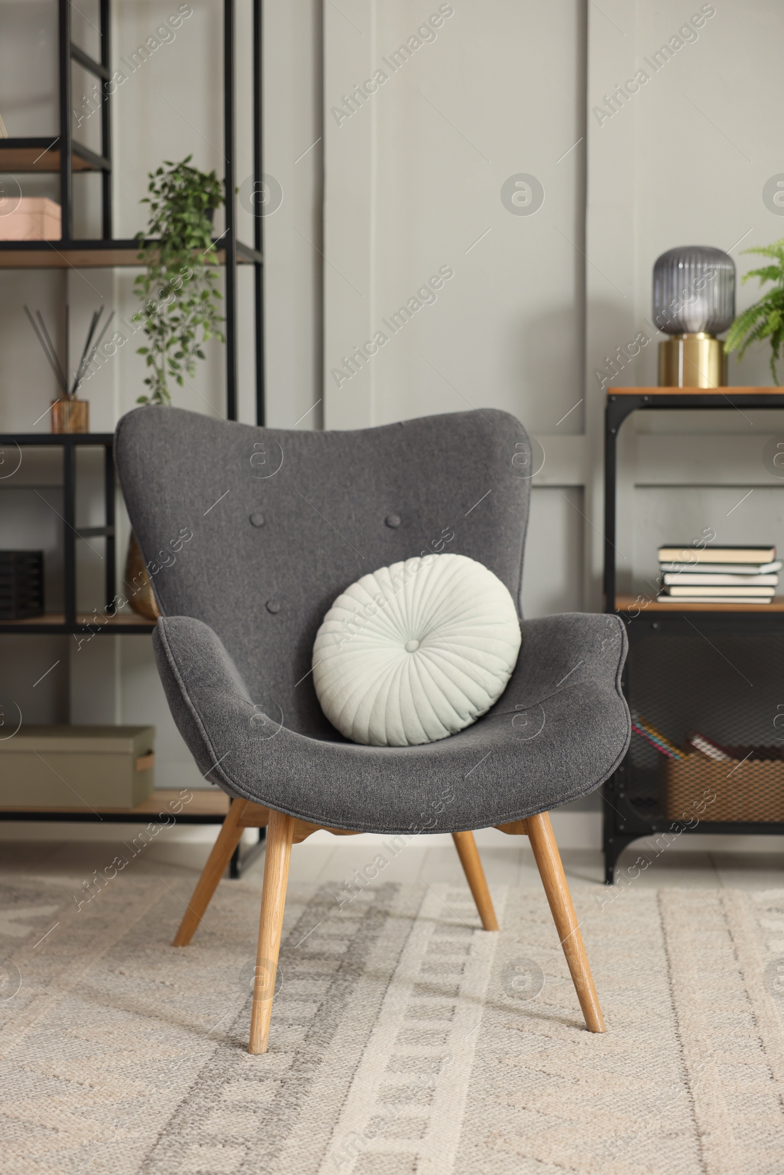 Photo of Stylish grey armchair with pillow and shelving unit indoors. Interior design