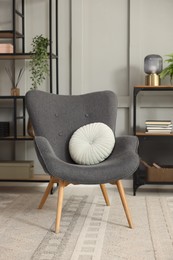 Photo of Stylish grey armchair with pillow and shelving unit indoors. Interior design
