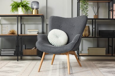Photo of Stylish grey armchair with pillow and shelving unit indoors. Interior design