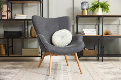 Photo of Stylish grey armchair with pillow and shelving unit indoors. Interior design