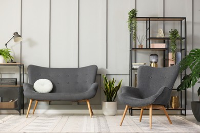 Photo of Stylish grey armchair, sofa, shelving unit and houseplants indoors. Interior design