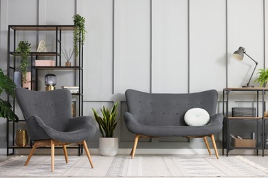 Photo of Stylish grey armchair, sofa, shelving unit and houseplants indoors. Interior design