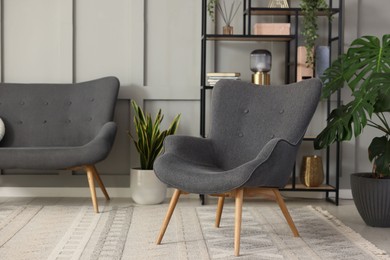 Photo of Stylish grey armchair, sofa, shelving unit and houseplants indoors. Interior design