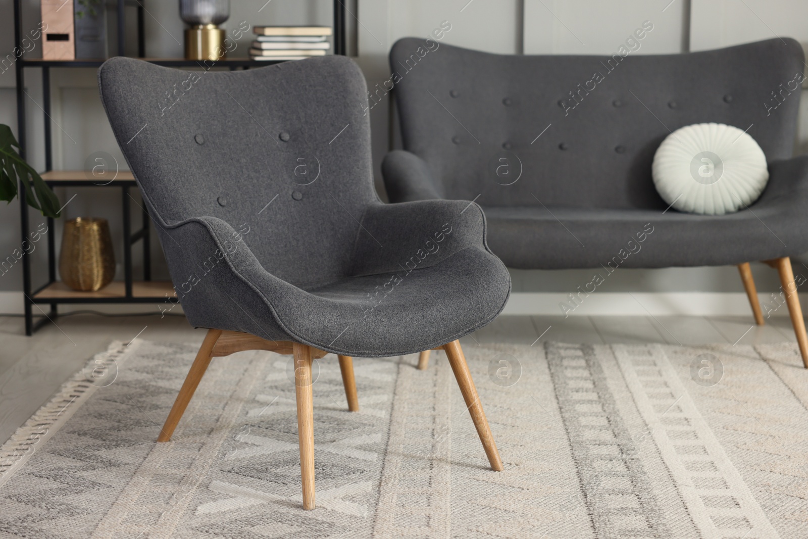 Photo of Stylish grey armchair, sofa and shelving unit indoors. Interior design