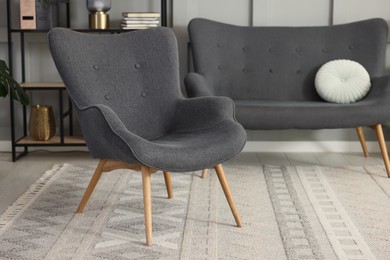 Photo of Stylish grey armchair, sofa and shelving unit indoors. Interior design