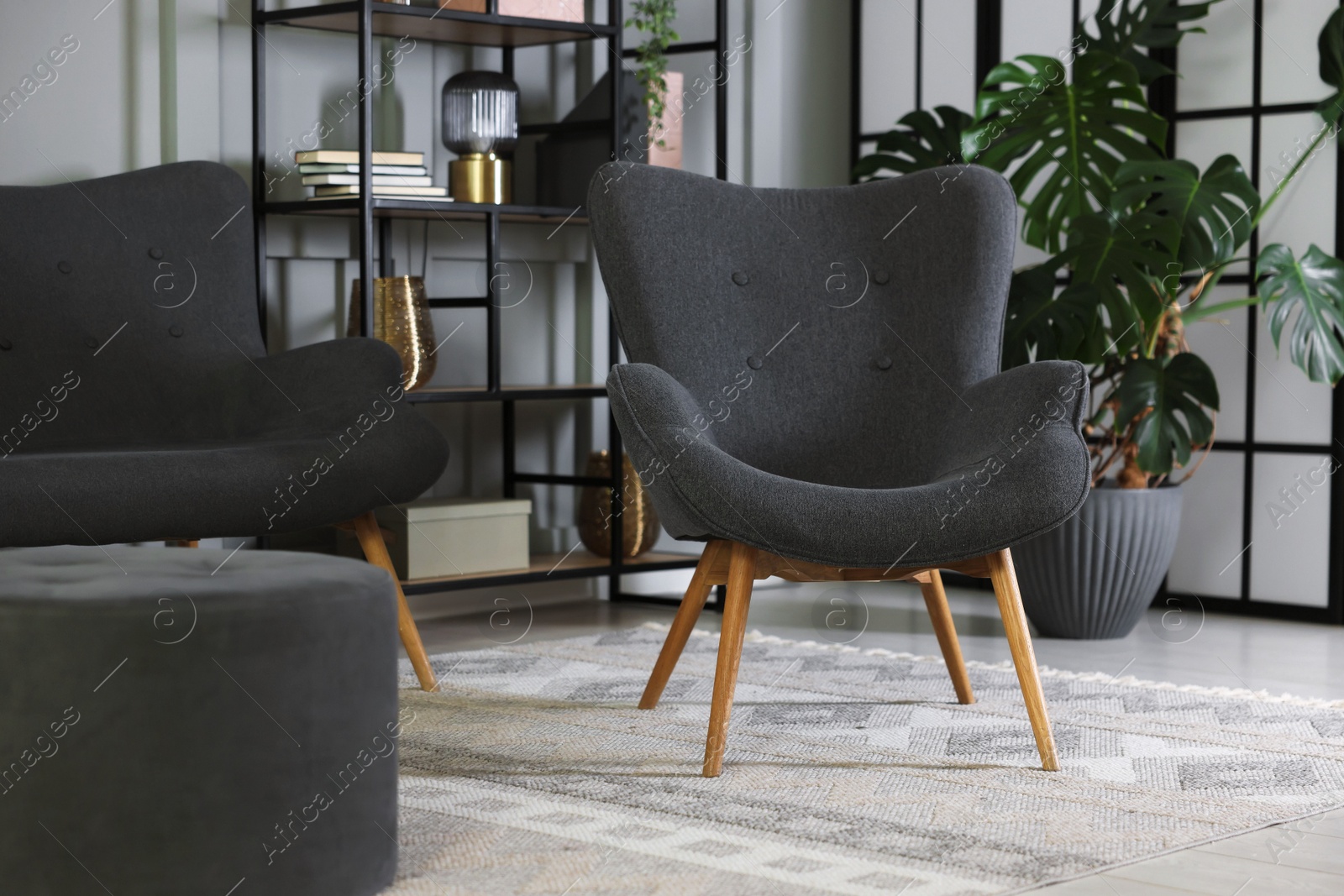 Photo of Stylish grey armchair, sofa and pouf indoors. Interior design
