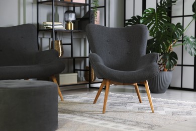 Photo of Stylish grey armchair, sofa and pouf indoors. Interior design