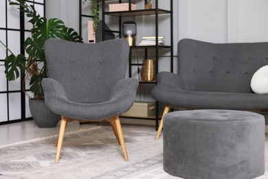 Photo of Stylish grey armchair, sofa and pouf indoors. Interior design