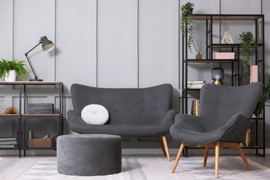 Photo of Stylish grey armchair, sofa, pouf, shelving unit and houseplants indoors. Interior design