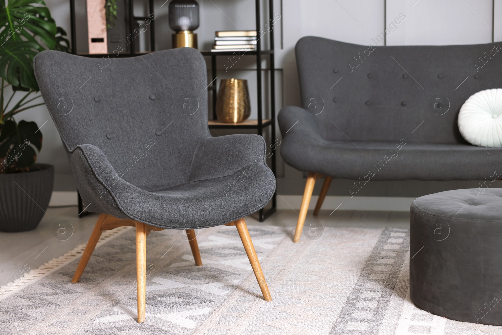 Photo of Stylish grey armchair, sofa and pouf indoors. Interior design