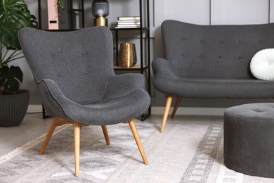 Photo of Stylish grey armchair, sofa and pouf indoors. Interior design