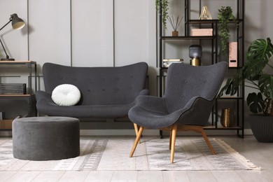 Photo of Stylish grey armchair, sofa, pouf, shelving unit and houseplants indoors. Interior design