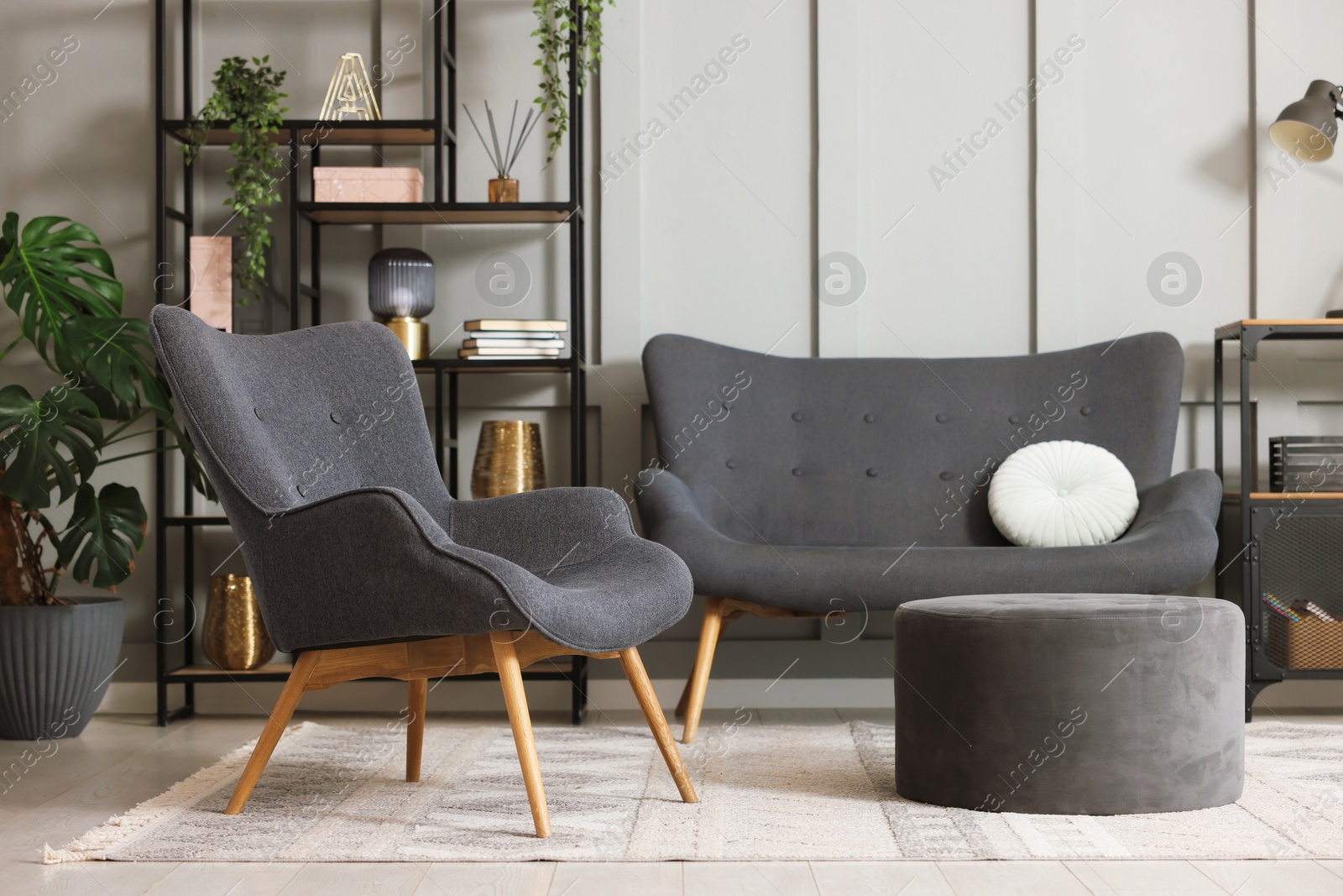 Photo of Stylish grey armchair, sofa, pouf, shelving unit and houseplants indoors. Interior design
