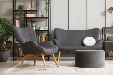 Photo of Stylish grey armchair, sofa, pouf, shelving unit and houseplants indoors. Interior design