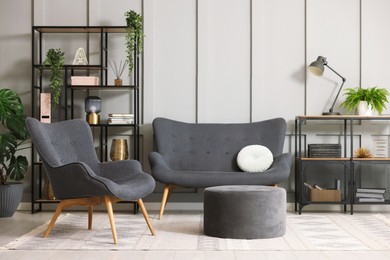 Photo of Stylish grey armchair, sofa, pouf, shelving unit and houseplants indoors. Interior design