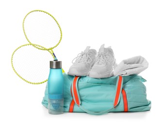 Photo of Stylish sports bag with badminton rackets, towel, bottle and sneakers isolated on white