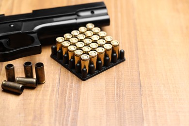 Photo of Bullets and gun on wooden table, closeup. Space for text