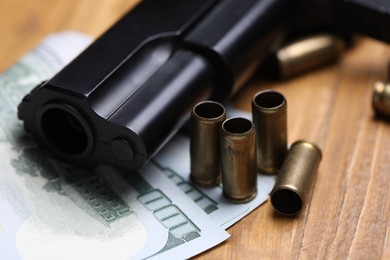 Photo of Bullets, dollars and gun on wooden table, closeup