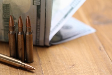 Photo of Bullets and dollars on wooden table, closeup. Space for text