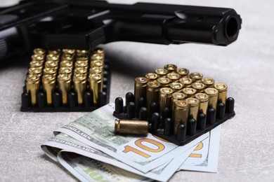 Photo of Bullets, gun and dollars on grey table, closeup