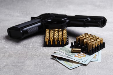 Photo of Bullets, gun and dollars on grey table, closeup