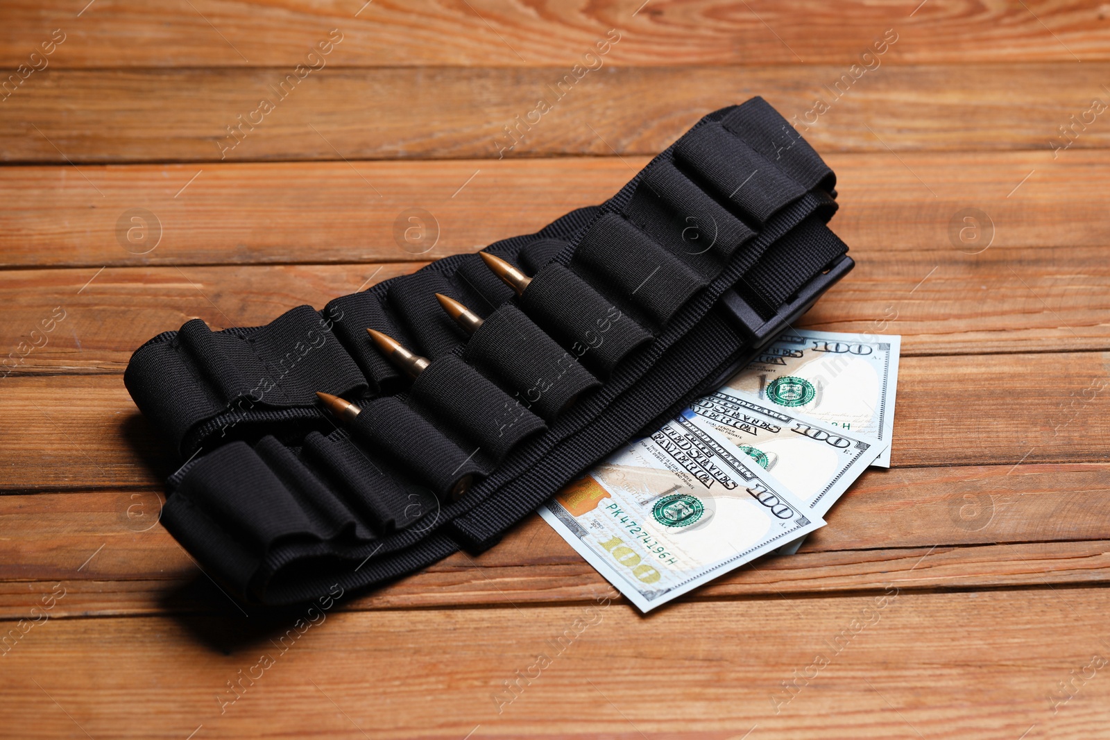 Black ammunition belt with bullets and dollars on wooden table Photo of Black ammunition belt with bullets and dollars on wooden table