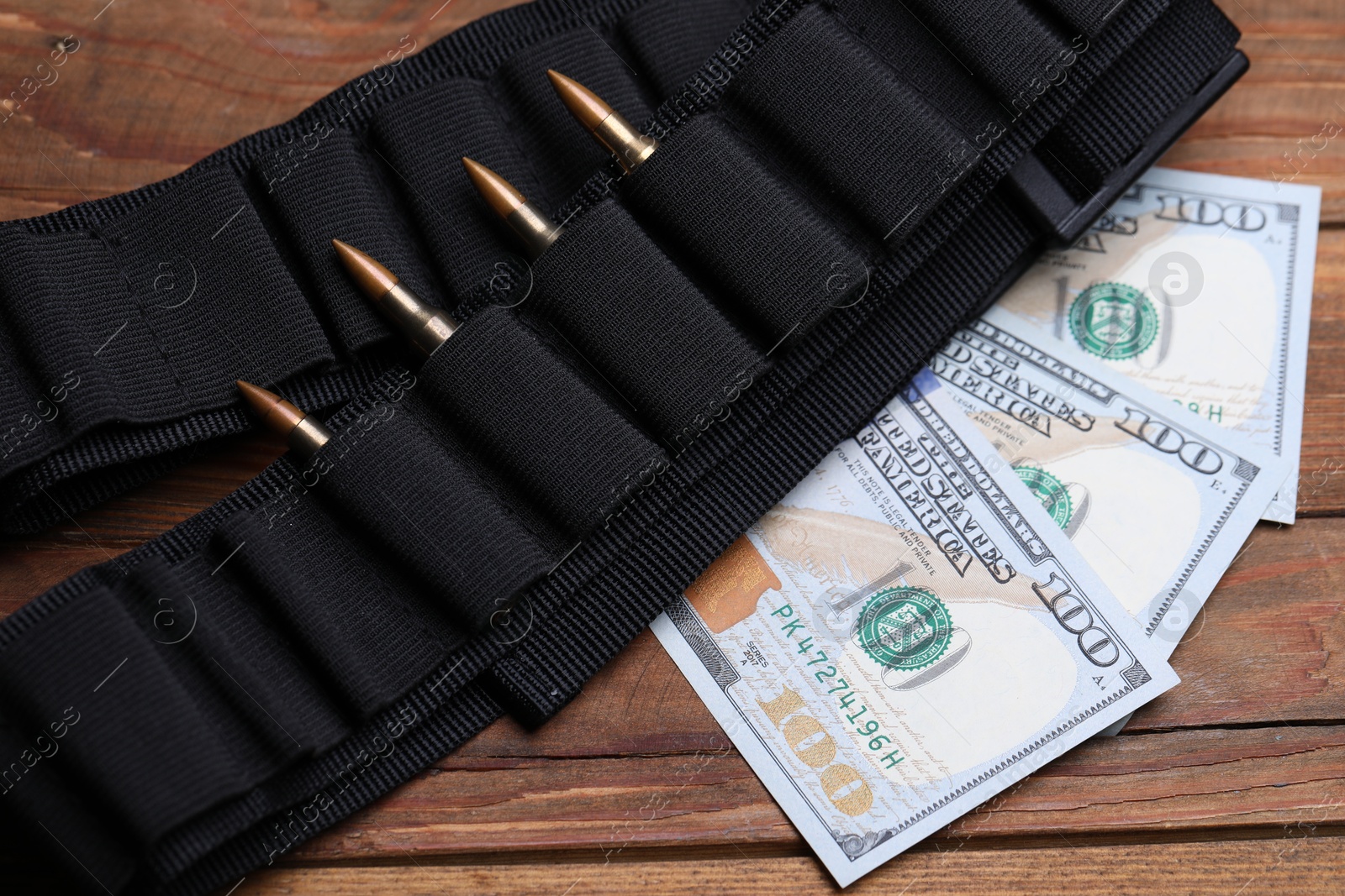 Black ammunition belt with bullets and dollars on wooden table, flat lay Photo of Black ammunition belt with bullets and dollars on wooden table, flat lay