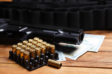 Photo of Bullets, gun, dollars and ammunition belt on wooden table, closeup