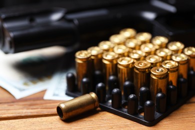 Photo of Bullets, gun and dollars on wooden table, closeup