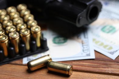 Photo of Bullets, gun and dollars on wooden table, closeup