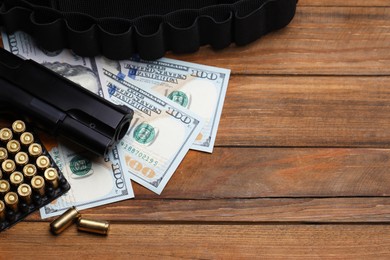 Photo of Bullets, gun, dollars and ammunition belt on wooden table, flat lay. Space for text