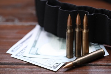 Photo of Many metal bullets, dollars and ammunition belt on wooden table, closeup