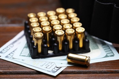 Photo of Many metal bullets, dollars and ammunition belt on wooden table, closeup